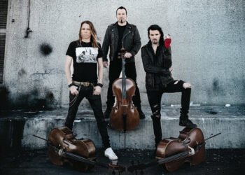 Apocalyptica posing in black clothing against a grey concrete wall, with three cellos placed around them