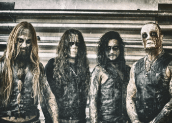 Belphegor band members in corpse paint and leather vests posing in front of a corrugated metal wall