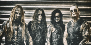 Belphegor band members in corpse paint and leather vests posing in front of a corrugated metal wall