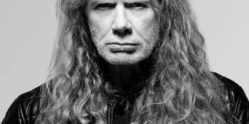 Black-and-white portrait of Dave Mustaine with long curly hair and a black leather jacket against a light grey background