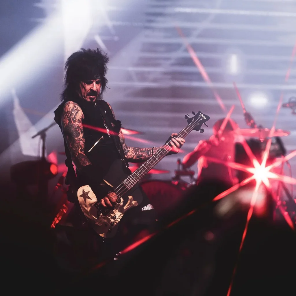 Nikki Sixx of Mötley Crüe playing a skull-and-star bass on stage under red and white lights.