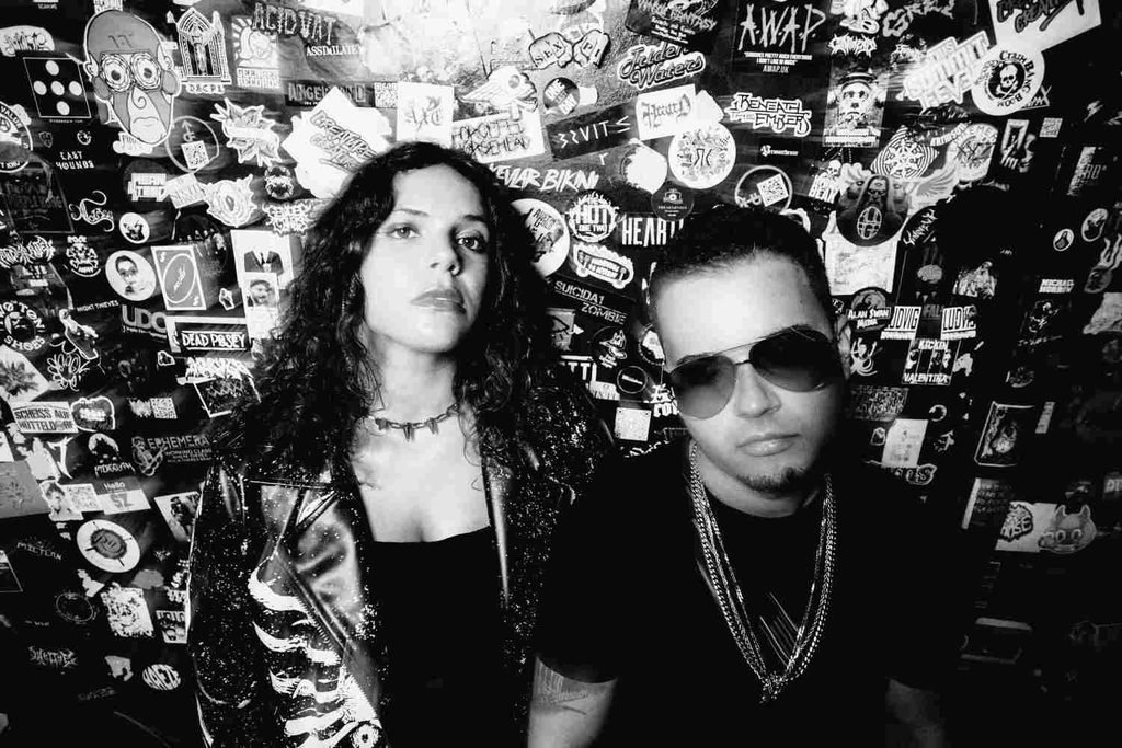 Black-and-white photo of Electron posing in front of a wall covered in band stickers.