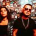 Electron in front of a sticker-covered wall, her in a skeleton-print jacket and him in sunglasses and chains