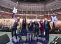 Iron Maiden celebrating on stage with guitars raised in front of a packed stadium crowd