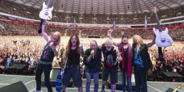 Iron Maiden celebrating on stage with guitars raised in front of a packed stadium crowd