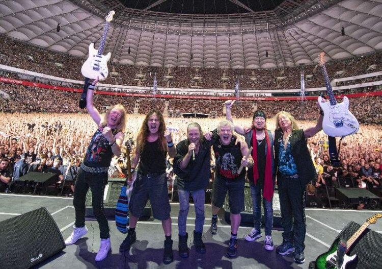 Iron Maiden celebrating on stage with guitars raised in front of a packed stadium crowd