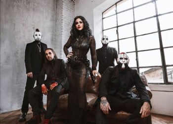 Lacuna Coil posing in black outfits and white face paint in a loft with an arched window, the singer standing at the center in a black lace gown.
