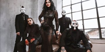 Lacuna Coil posing in black outfits and white face paint in a loft with an arched window, the singer standing at the center in a black lace gown.